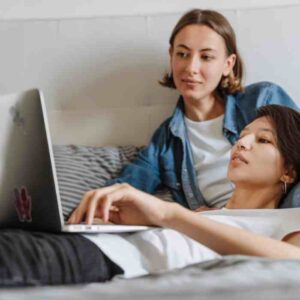 A blog from Schuggies Ceilidhs. Countdown to ‘I Do’ – Last Minute Wedding Preparations Made Easy. This image represents an LGBTQ couple settling outstanding payments from a laptop on a comfy looking bed.
